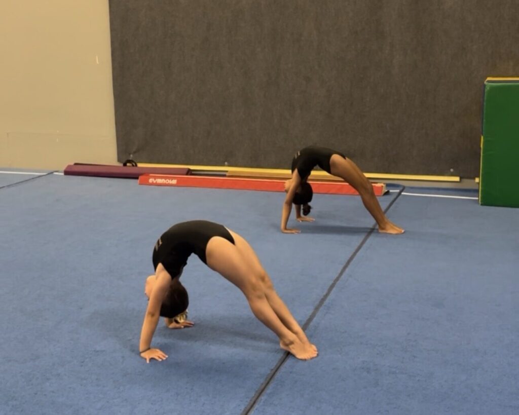 Two girls doing bridges on floor with straight legs.